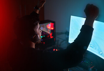 Man in dark room, video game win with fist pump and online streaming, gaming competition and esports on computer. Achievement, cyber and male streamer celebrate winning gamer tournament with success © Samir H/peopleimages.com