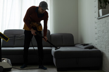 Dry cleaner's man employee removing dirt from furniture in flat, closeup, vacuum clean sofa with professional equipment.
