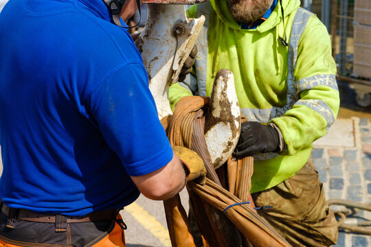 workers in hi-vis and hard hats unhook lifting chain from heavy crane hook