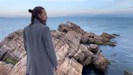 a man in a gray coat stands near  sea cliff