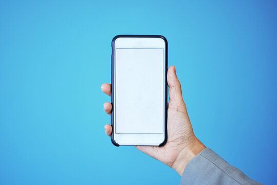Person, phone and hand with mockup screen for advertising or marketing against a blue studio background. Hands, mobile smartphone or app with mock up, copy space or display for brand advertisement