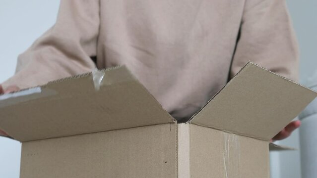 Close up hands unpacking a parcel, looking inside the open a cardboard box at home near the door. Post delivery