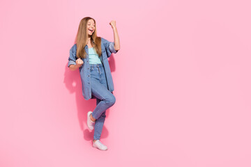 Full length photo of attractive young teenager woman raise fists scream hooray wear trendy jeans clothes isolated on pink color background