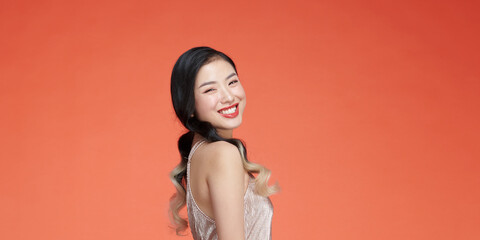 Attractive asian young woman standing on red background, wearing silver evening dress