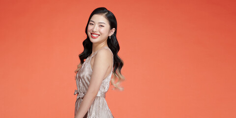 Attractive asian young woman standing on red background, wearing silver evening dress
