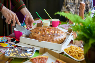 A hand cuts a pie with a knife. A lush pie with a filling on a festive table with food.
