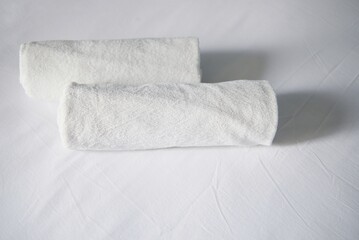 A pair of white towels on a white bedsheet in a bedroom