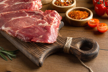 Fresh meat steaks on a wooden board, spices, rosemary. Free space for text