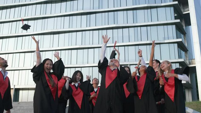 High university graduates rejoice at the end of their studies, people of different ages and races in capes of graduates they throw hats in the air near the modern university, slow motion.