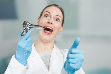 Female gynecologist makes funny gestures with a speculum to take away the fear - obrazy, fototapety, plakaty
