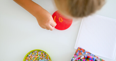 Little girl makes figure from bead on the table at home, top view