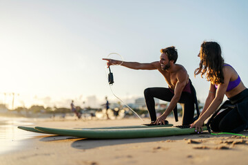 A surf instructor is pointing at good wave while a girl smiling and watching.