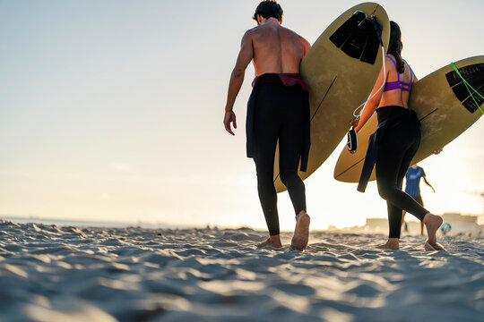 Rear view of couple of surfers carry surfboards on the beach.