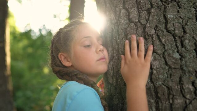 a small child ecologist hugs the trunk of a tree bark in a forest park. the gentle touch of a child on the trunk of the tree of life. Nature in caring hands: children lifestyle protect the forest