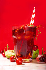 Iced cherry cola drink, Cold summer fruity non-alcohol cocktail with fresh cherries, juice, cola and ice, on high-colored background copy space