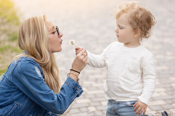 Young mother plays with her little son in the park. Dandelions pick flowers and blow