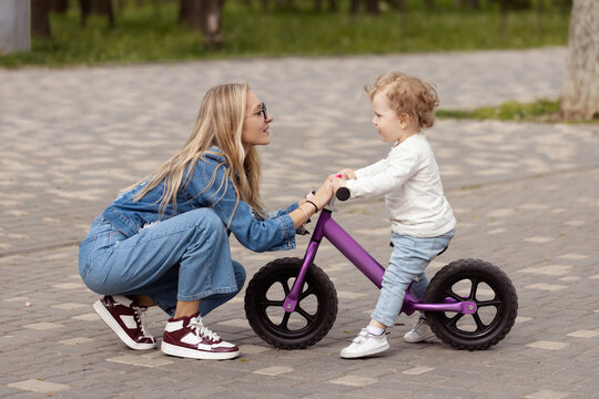 Young mother teaches her little son how to ride a balance bike in the park