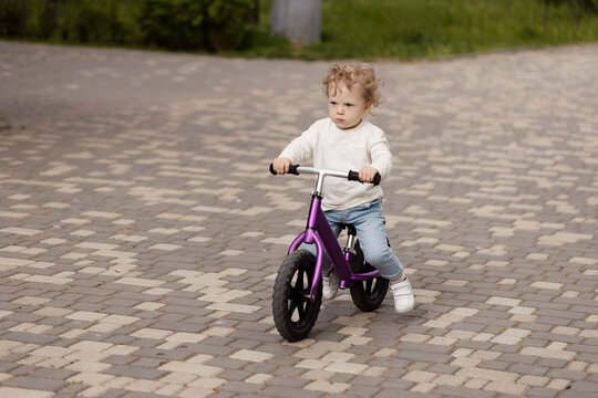 Cute little smiling child learning to ride a balance bike in the park