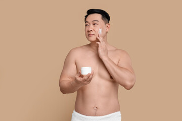 Fototapeta premium Handsome man applying cream onto his face on light brown background