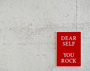 Red poster on copy space white wall with message DEAR SELF YOU ROCK, concept of positive self talk...