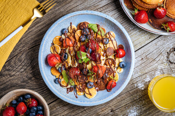 Small American pancakes mixed with seasonal fruit like strawberries, blueberries and cherries. Dipped with melted chocolate, placed on a rustic wooden board. 