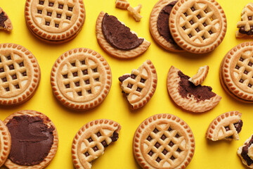 Tasty sandwich cookies with cream on yellow background, flat lay