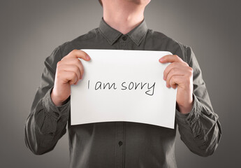 Apology. Man holding card with phrase I Am Sorry on grey background, closeup