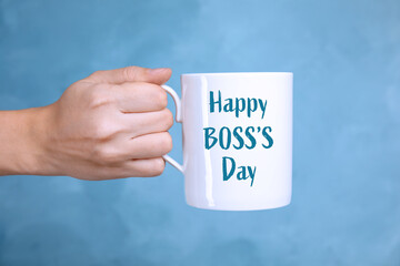 Woman holding mug with phrase Happy Boss`s Day on light blue background, closeup