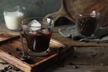 Glass of delicious iced coffee and beans on wooden table, space for text