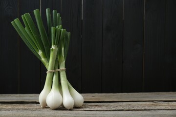 Bunch of fresh green spring onions on wooden table, space for text