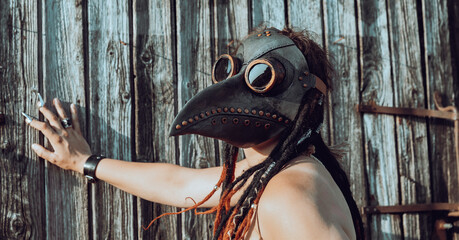 Nude woman with plague raven mask near old wooden fence