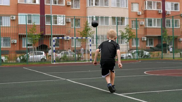 A boy trains with a soccer ball on a rubber-coated playground in the yard. The child hits the goal with a ball.
