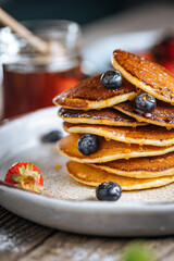 American pancakes with blueberries, strawberries and cherries with dip of honey. Placed on a rustic designer plate, on wooden rustic board. 
