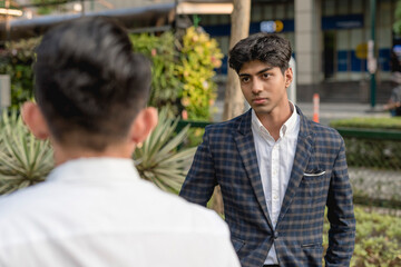 A hotheaded young indian man stares down his workmate while outside the office. Animosity in the workplace. - obrazy, fototapety, plakaty
