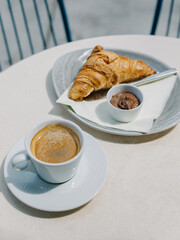 Cup of black coffee and a croissant on a table in a street cafe.