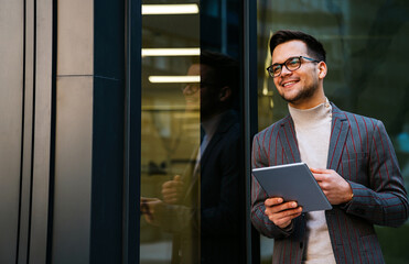 Happy young business man with tablet at work in modern urban background