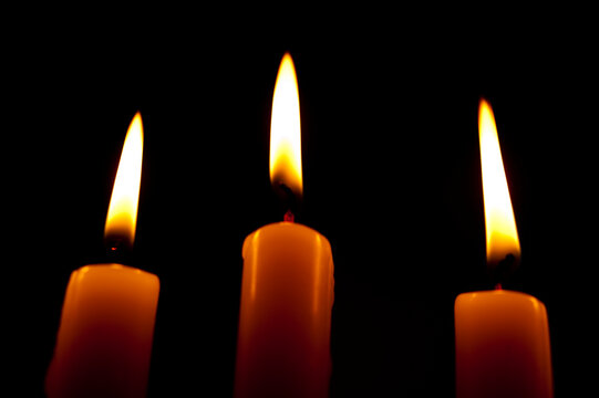 Beautiful image with 3 lighted candles with white and yellowish flames on a black background