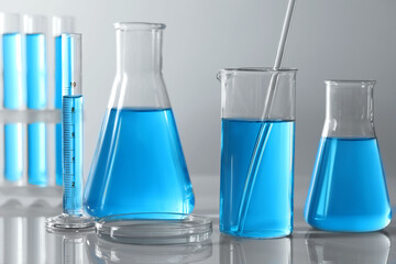 Different laboratory glassware and test tubes with light blue liquid on table