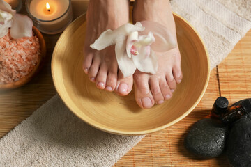 Woman soaking her feet in bowl with water and flower, closeup. Pedicure procedure