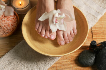 Obraz na płótnie Canvas Woman soaking her feet in bowl with water and flower, closeup. Pedicure procedure