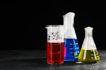 Laboratory glassware with colorful liquids on dark table against black background, space for text....