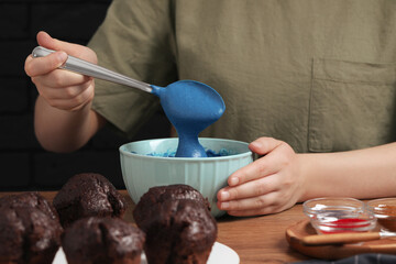 Woman mixing cream with blue food coloring at wooden table, closeup
