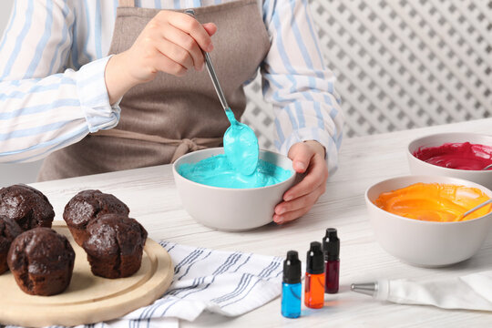Woman mixing cream with light blue food coloring at white wooden table, closeup. Decorate cupcakes