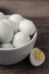 Many peeled hard boiled quail eggs in bowl on wooden table, closeup