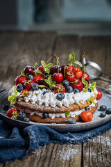Fresh seasonal layered cake with spring ripe fruit like strawberries, blueberries and cherries. Placed on a elegant blue plate on rustic wooden board
