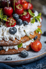 Fresh seasonal layered cake with spring ripe fruit like strawberries, blueberries and cherries. Placed on a elegant blue plate on rustic wooden board