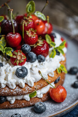 Fresh seasonal layered cake with spring ripe fruit like strawberries, blueberries and cherries. Placed on a elegant blue plate on rustic wooden board