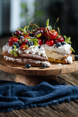 Fresh seasonal layered cake with spring ripe fruit like strawberries, blueberries and cherries. Placed on a elegant blue plate on rustic wooden board