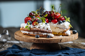 Fresh seasonal layered cake with spring ripe fruit like strawberries, blueberries and cherries. Placed on a elegant blue plate on rustic wooden board
