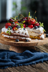 Fresh seasonal layered cake with spring ripe fruit like strawberries, blueberries and cherries. Placed on a elegant blue plate on rustic wooden board